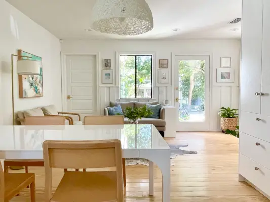 Vue vers le coin salon avec table à manger moderne blanche et chaises en bois