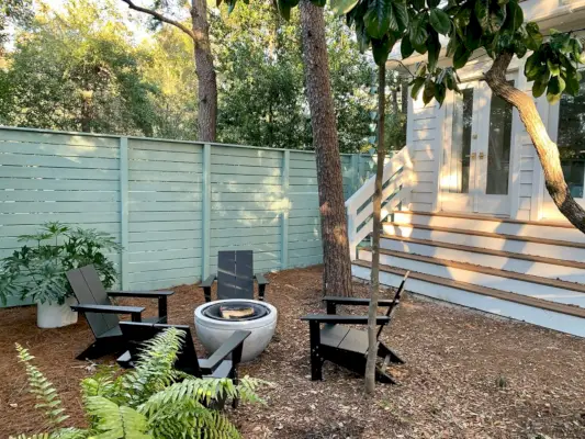 Zone de foyer avec chaises Adirondack noires devant une clôture verte