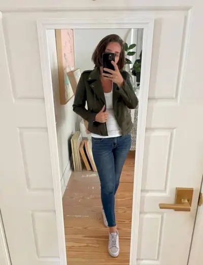 Sherry selfie dans un miroir à la maison avec un débardeur blanc et une veste verte avec un jean et des chaussures de tennis