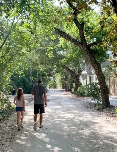 Joan i la filla passejant per un barri cobert d'arbres