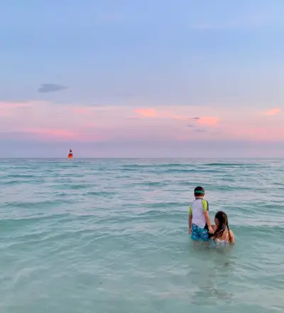 Enfants jouant dans le golfe du Mexique au coucher du soleil avec voilier en arrière-plan