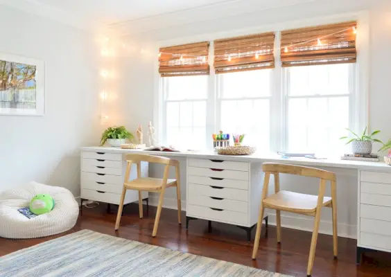 Sala de arte para niños con dos sillas de madera a lo largo de un espacio de trabajo de escritorio de arte largo con luces de cadena