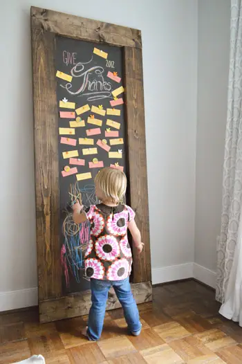 Menina pequena desenhando em um quadro-negro inclinado DIY com notas de gratidão do Dia de Ação de Graças