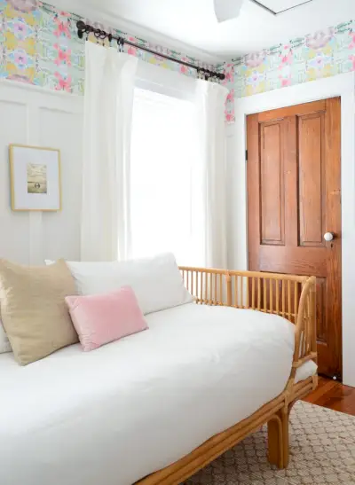 Espreguiçadeira de vime com roupa de cama branca em quarto com portas de madeira