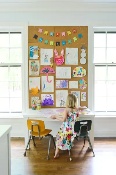 arte infantil exibida em uma grande parede de cortiça no escritório doméstico acima da mesa de arte infantil