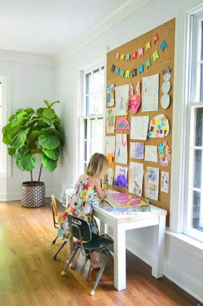 kind werkt aan kunst onder een gigantische muur van kurkbord met tekeningen en schilderijen opgespeld