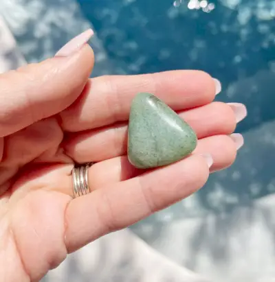 Mano que sostiene la piedra preciosa pulida de aventurina verde sobre el agua