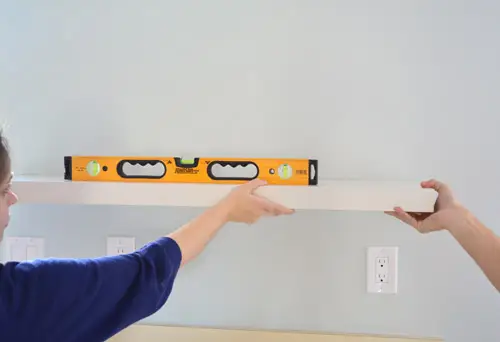 usando un nivel para marcar la ubicación de los estantes flotantes de Ikea en la pared de la cocina