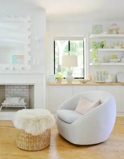 Dormitorio playero blanco con silla giratoria West Elm junto a la chimenea