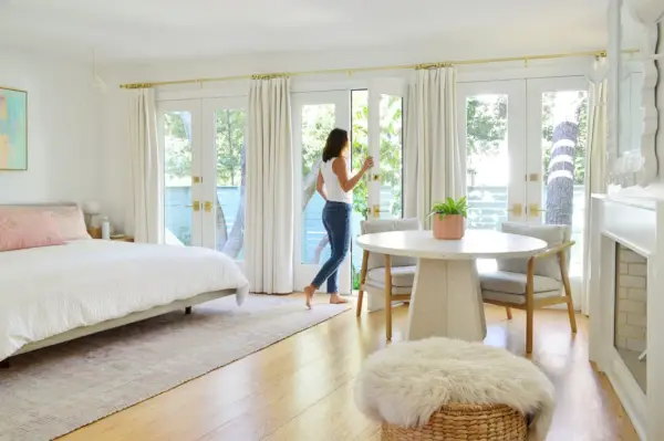 Mujer caminando a través de la pared de puertas francesas en un luminoso dormitorio playero