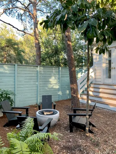 Arbres autour de la cour latérale clôturée avec chaises Adirondack noires autour du foyer