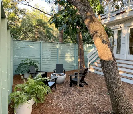 Cortile laterale verde recintato con sedie Adirondack nere attorno al pozzo del fuoco