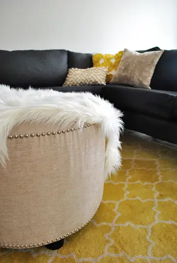 grand pouf rond rembourré avec garniture de tête de clou sur un tapis de grange en poterie jaune