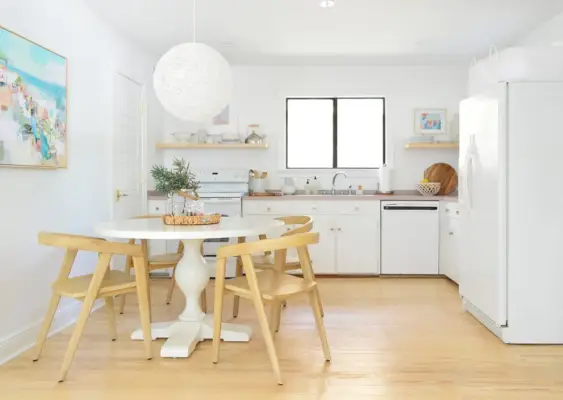 Cozinha minimalista com mesa de pedestal de armários brancos e luminária pendente globo com cadeiras de madeira