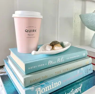 Gros plan d'une pile de livres bleus avec une tasse à café Pink Quirk Hotel