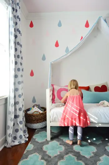 Fille jouant sur le lit sous la fresque murale finale en forme de goutte de pluie sur un lit à baldaquin en tissu