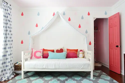 Chambre de filles avec une fresque murale colorée autour d'un lit de repos à baldaquin avec porte de placard ouverte