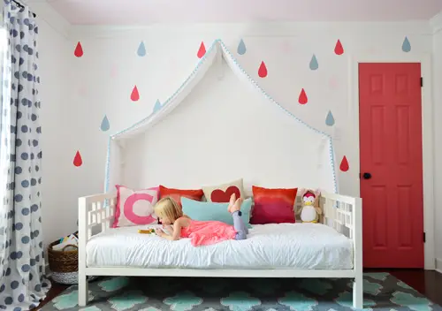 Après la photo d'une fille lisant sur un lit de repos avec un auvent en tissu, une porte colorée et une fresque murale en forme de goutte de pluie