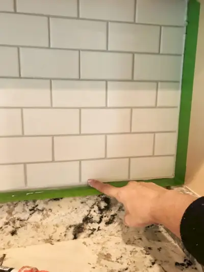 Sherry espalhando calafetagem com o dedo ao longo das bordas do backsplash instalado