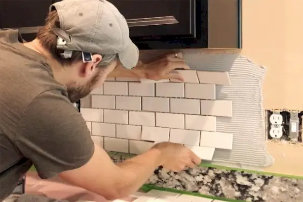 John colocando uma folha branca de ladrilho de metrô em mastique para definir backsplash