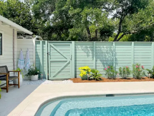 Valla de piscina con listones horizontales y pintura verde grisácea con parterre en frente