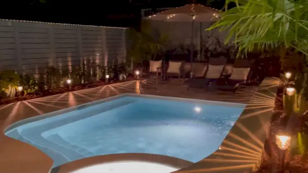 Petite piscine de forme libre la nuit avec lumières de piscine et lampes solaires allumées