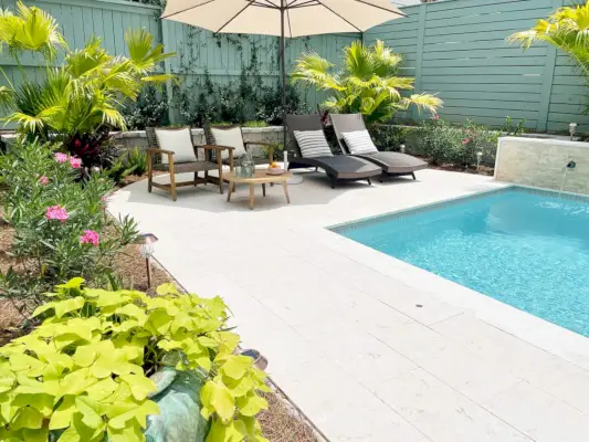 Piscina en el patio trasero con área para sentarse bajo una sombrilla rodeada de plantas tropicales