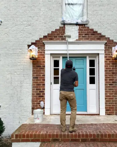 Peintre peignant le porche d'une maison en brique blanche