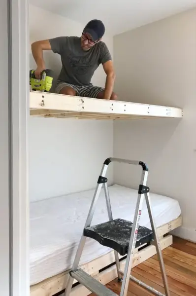 John sentado en la litera superior para clavar madera contrachapada en una plataforma flotante