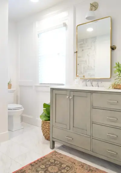 Relooking de salle de bain avec vanité grise installée avec miroir en laiton et moulure murale décorative