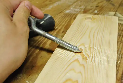 raspar el tornillo a lo largo de una nueva tabla de madera para crear un efecto desgastado para un proyecto de bricolaje