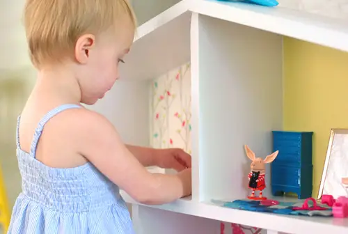 Nahaufnahme eines kleinen Mädchens, das mit Olivia Pig-Figuren in einem selbstgebauten Puppenhaus spielt