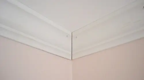 Coin de moulure couronnée installé contre le plafond avec un petit joint au coin à calfeutrer