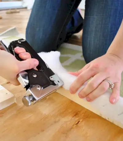 Usando una pistola de grapas para colocar guata en la parte posterior de una cabecera de tela tapizada de bricolaje