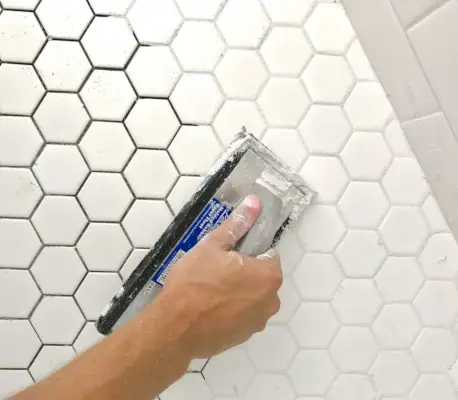 Espalhando argamassa em ladrilho hexagonal branco com flutuador de argamassa