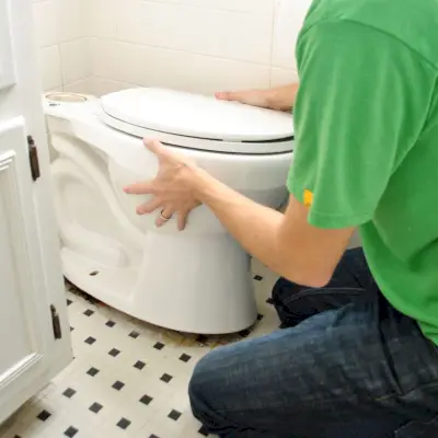 John fait basculer la vieille cuvette des toilettes pour desserrer l'anneau de cire