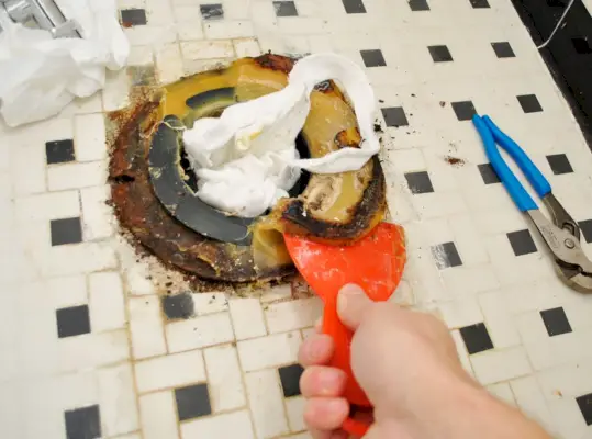 Gratter le vieil anneau de cire du sol de la salle de bain pendant l'installation des toilettes