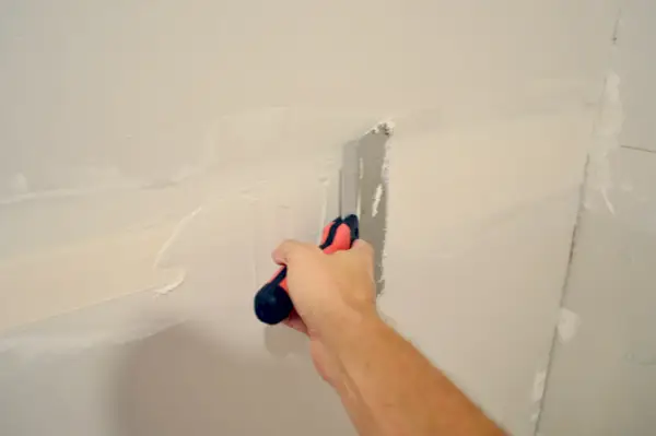 faca maior de drywall sendo arrastada pela fita para aplicar outra camada de lama