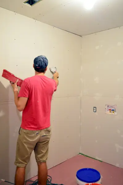 John aplicando lama sobre marcas de cabeça de parafuso de drywall