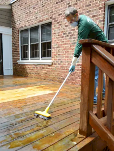 John schrubbt das Holzdeck, um die alte Lackierung mit einer harten Bürste zu entfernen