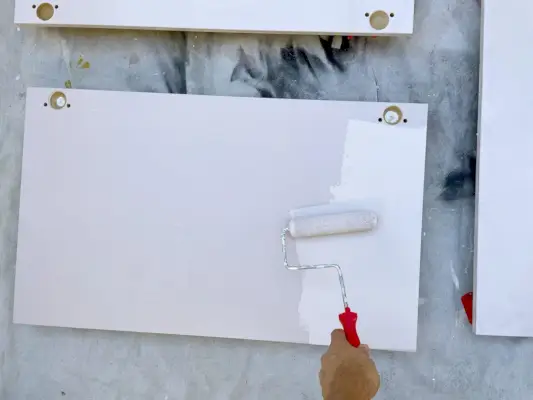 Appliquer de la peinture rose sur les portes d'armoires de cuisine Ikea avec un petit rouleau en mousse