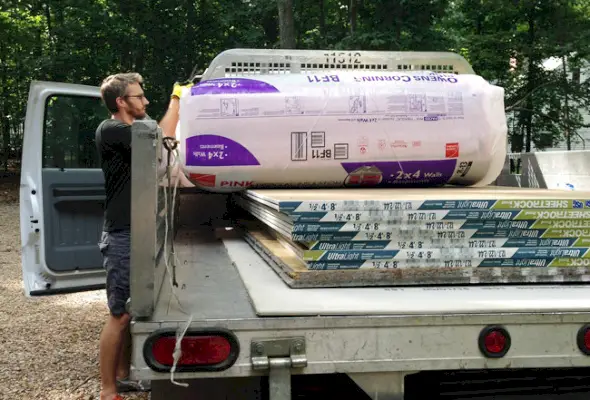 John soulève l'isolant de la plate-forme du camion avec des plaques de plâtre à l'arrière également