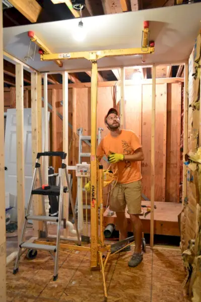 John utilise un élévateur pour cloisons sèches pour maintenir la plaque de plâtre au plafond