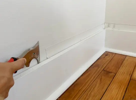 Gratter le vieux calfeutrage pour un mur lisse au-dessus des plinthes