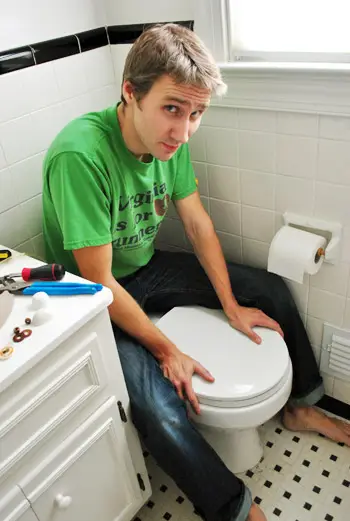 John oefent druk uit op de toiletbeugel om de wasring op zijn plaats te houden