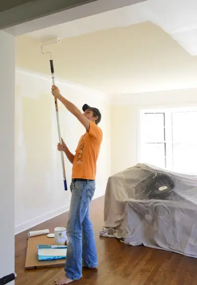 John appliquant de la peinture au plafond avec un rouleau sur une rallonge