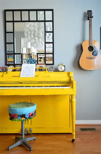 Helder geel geschilderde piano in muziekkamer met gitaar op de muur