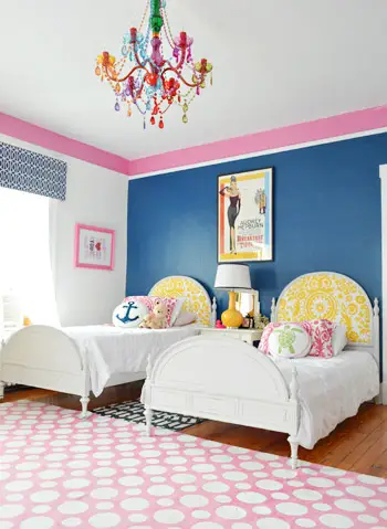 Twin bed naast elkaar in blauwe kamer met roze rand en kleurrijke kristallen kroonluchter