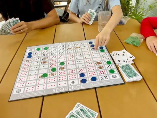 Familie spielt Sequenz-Brettspiel auf Tisch im Freien