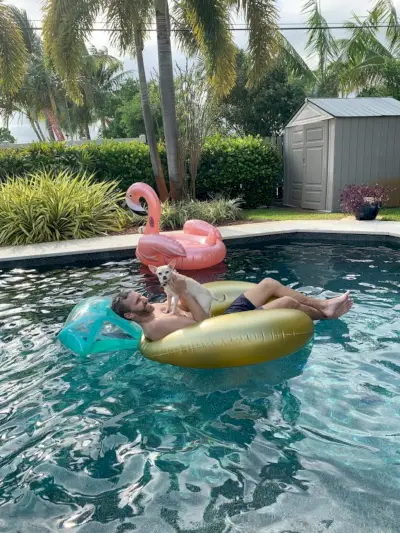 John dans la piscine flotte avec Burger sur la poitrine avec un flotteur flamant rose en arrière-plan